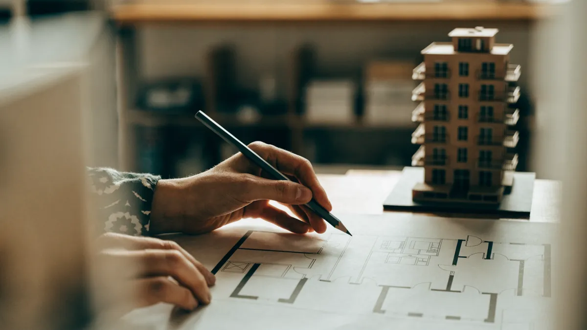 Hands marking an apartment floor plan with a pencil beside a scale model of a residential building